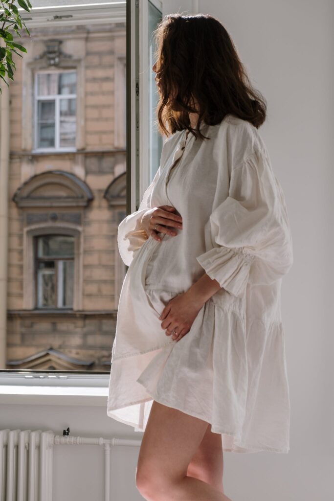 Pregnant Woman in White Dress Near a Window